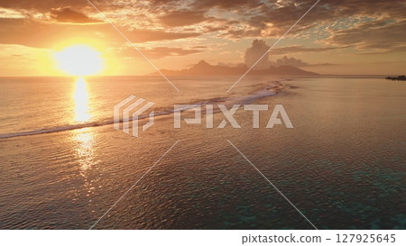 Golden sunset over the ocean illuminating a tropical island in French Polynesia, creating a breathtaking view of the coastline, waves, and the distant mountains 127925645
