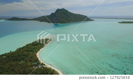 Aerial view of Bora Bora lagoon showing mount Otemanu, lush tropical vegetation, turquoise water, coral reef, and white sand beach in French Polynesia 127925658