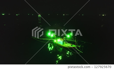 Aerial view capturing traditional Thai fishing boats illuminated by green lights to attract squid at night, creating a mesmerizing scene on calm waters near Koh Phangan Island 127925670