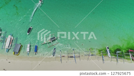 Aerial view of White Beach in Boracay, Philippines, featuring iconic paraw sailboats in turquoise waters, with a speedboat enhancing the vibrant tropical scene Aerial view of White Beach in Boracay, Philippines, featuring iconic paraw sailboats in turquoise waters, with a speedboat enhancing the vibrant tropical scene 127925675