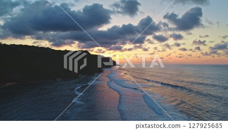 Soft waves rolling gently toward the shore at sunset along the stunning Bali coast in Indonesia, with dramatic clouds enhancing the breathtaking scenic beauty of the landscape Soft waves rolling gently toward the shore at sunset along the stunning Bali coast in Indonesia, with dramatic clouds enhancing the breathtaking scenic beauty of the landscape 127925685