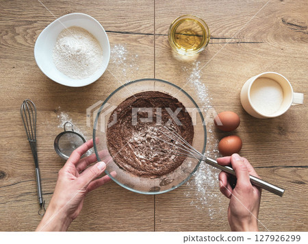 A woman prepares chocolate dough at a wooden table, top view. 127926299