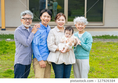 A group photo of a smiling three-generation family surrounding a baby in front of their home 127926384