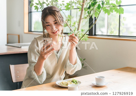 Young Asian woman looking at her smartphone while having lunch in a cafe 127926919