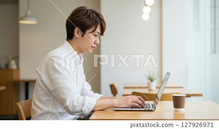 A young man concentrating on his work using a laptop in a cafe 127926971