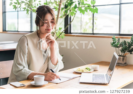 Young Asian woman teleworking while eating in a cafe Young Asian woman teleworking while eating in a cafe 127927239