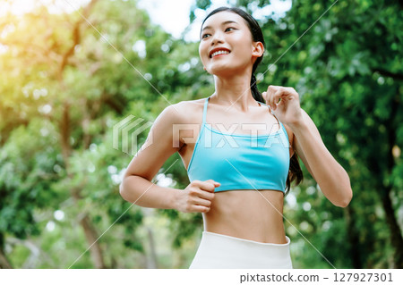 Close-up of an Asian woman jogging outdoors with a confident and focused expression 127927301