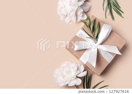 Gift box and peony flowers on beige background Gift box and peony flowers on beige background 127927616