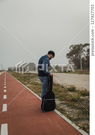 Musician Waiting For The Bus With His Guitar In Case Musician Waiting For The Bus With His Guitar In Case 127927703
