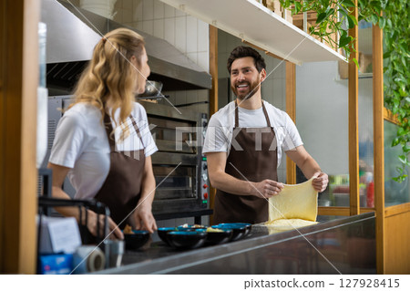 Man and woman in brown aprons preparing pizza dough in kitchen 127928415