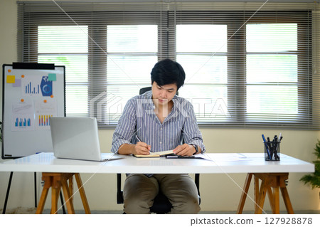 Focused financial analyst reviewing data and preparing documentation in bright office 127928878