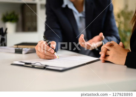Two businesspeople in suits finalizing an important business deal at a modern office desk Two businesspeople in suits finalizing an important business deal at a modern office desk 127928893