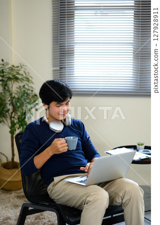Relaxed male freelancer enjoying a hot drink while using his laptop at home Relaxed male freelancer enjoying a hot drink while using his laptop at home 127928911