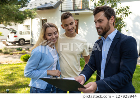 Real estate agent presenting clipboard with documents to couple in front of residential property Real estate agent presenting clipboard with documents to couple in front of residential property 127928944