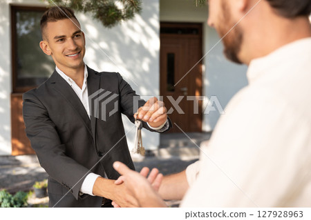 Real estate agent handing over house keys to client in front of residential property during property Real estate agent handing over house keys to client in front of residential property during property 127928963