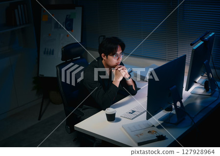 Focused businessman working late night on desktop computer in dark office 127928964