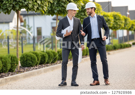 Builders discussing plans with technology outdoors 127928986