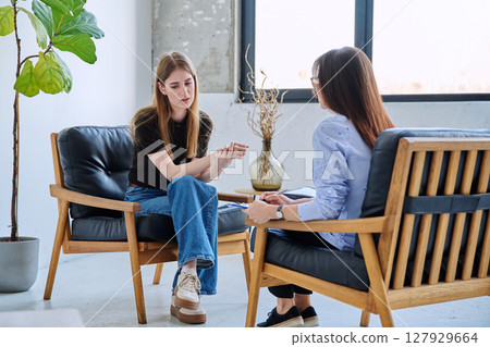 Serious teen girl in session in office of professional psychologist, therapist 127929664