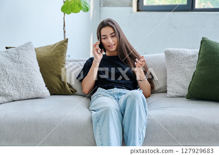Young woman sitting at home on couch talking on smartphone 127929683