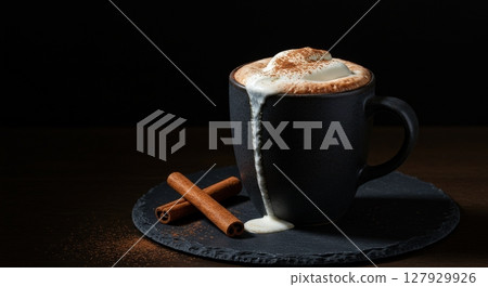 Hot cappuccino with whipped cream and cinnamon sticks in a dark mug on a black stone plate 127929926