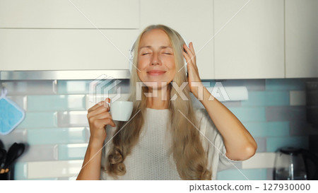 happy smiling woman listening to music with headphones enjoying hot tasty cup of coffee at home happy smiling woman listening to music with headphones enjoying hot tasty cup of coffee at home 127930000