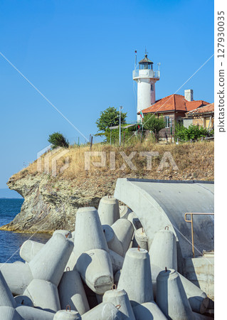 Lighthouse stand above concrete wave breakers along rocky coast under clear blue sky. Saint Anastasia Island in Burgas bay, Bulgaria. Concept of lighthouse, shoreline defense Lighthouse stand above concrete wave breakers along rocky coast under clear blue sky. Saint Anastasia Island in Burgas bay, Bulgaria. Concept of lighthouse, shoreline defense 127930035