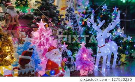 Luminous reindeer and Santa Claus figures illuminating colorful Christmas trees 127930220