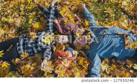 Family enjoying a beautiful fall day, lying on vibrant, colorful leaves in a park, embracing togetherness and the joy of nature Family enjoying a beautiful fall day, lying on vibrant, colorful leaves in a park, embracing togetherness and the joy of nature 127930246