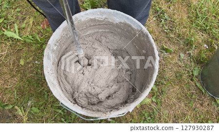 Construction worker mixing cement in bucket using mixing drill Construction worker mixing cement in bucket using mixing drill 127930287