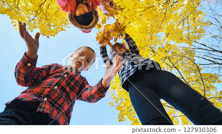 Family enjoying autumn park, holding yellow maple leaves from low perspective 127930306