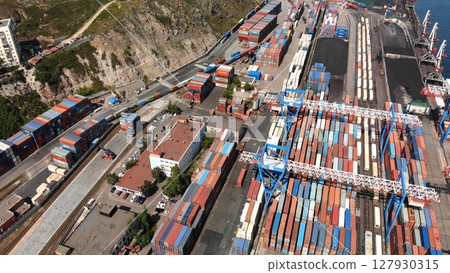 Industrial cargo port with cranes loading colorful shipping containers onto train cars, aerial view of global logistics and transportation hub 127930315