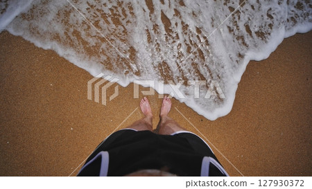 Tourist standing on Crimean beach enjoying foamy wave washing his feet 127930372