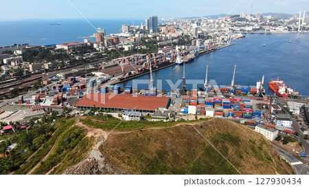 Cargo ships are docking and unloading at the commercial sea port in vladivostok, russia, with containers and cranes visible Cargo ships are docking and unloading at the commercial sea port in vladivostok, russia, with containers and cranes visible 127930434