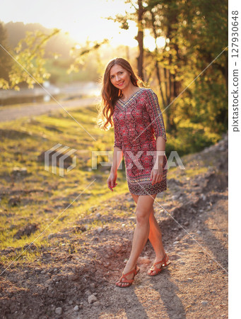 Portrait of young woman in casual summer dress, strong sunset backlight with nice bokeh, blurred trees and river background 127930648