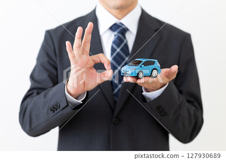A middle-aged male businessman in a suit holding a model of a car and making a circle sign A middle-aged male businessman in a suit holding a model of a car and making a circle sign 127930689