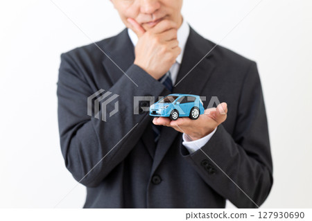 A middle-aged male businessman in a suit worried about a model car A middle-aged male businessman in a suit worried about a model car 127930690