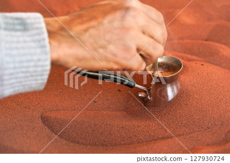 Coffee prepared on street in traditional Arabic way, cezve or ibrik (small Turkish coffe pot) is placed inside red hot sand until liquid boils, detail on local man hand stirring drink 127930724