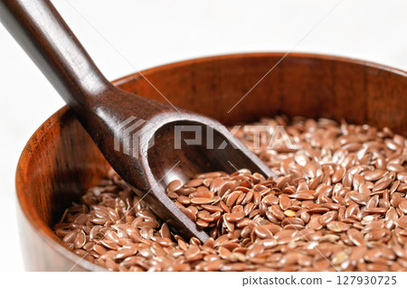 Common flax linseed in small wooden bowl with wooden scoop, closeup detail 127930725