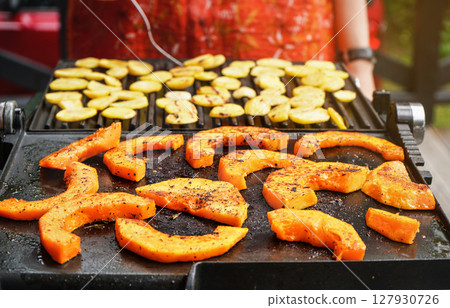 Bright orange butternut squash pieces seasoned with spices grilled on electric grill, blurred potato chips prepared in background Bright orange butternut squash pieces seasoned with spices grilled on electric grill, blurred potato chips prepared in background 127930726