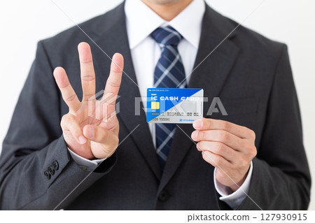 A middle-aged male businessman in a suit holding a bank's IC cash card and raising three fingers 127930915