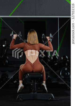 Determined sportswoman lifting dumbbells while sitting on bench in gym 127931316