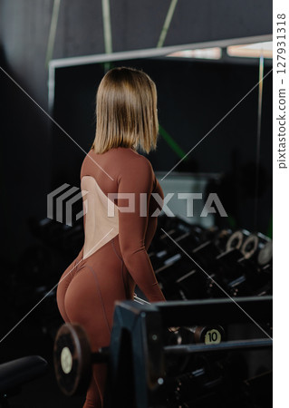 Fitness model wearing brown jumpsuit exercising in the gym Fitness model wearing brown jumpsuit exercising in the gym 127931318