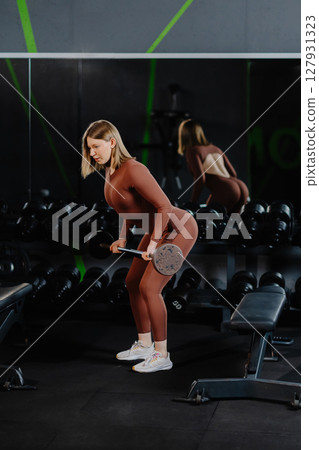 Athletic woman lifting barbell in gym showing back muscles 127931323