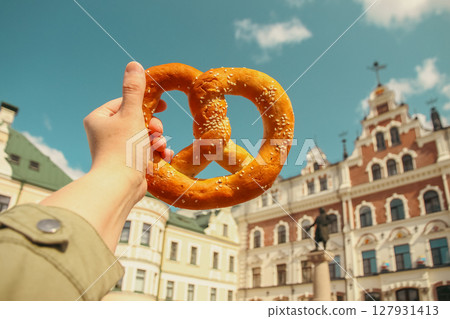 Traditional pretzel pastry in hand against the backdrop of Vyborg Town Hall on sunny day on sunny day 127931413