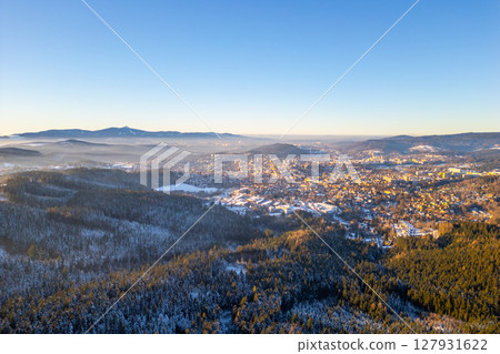A winter evening in Jablonec nad Nisou reveals a stunning view of the snow-covered city amidst the Jested Mountain Ridge. The warm hues of sunset cast a serene glow across the landscape. A winter evening in Jablonec nad Nisou reveals a stunning view of the snow-covered city amidst the Jested Mountain Ridge. The warm hues of sunset cast a serene glow across the landscape. 127931622