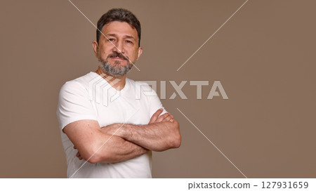 Confident man with crossed arms wearing white shirt against plain brown background Confident man with crossed arms wearing white shirt against plain brown background 127931659