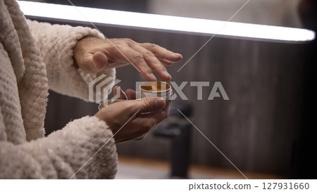 Cozy evening skincare routine with applying cream in warm, dimly lit home environment 127931660