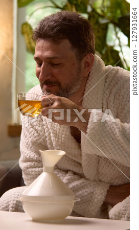 Lifestyle and wellness. Man enjoying hot beverage in cozy morning setting with plants in background Lifestyle and wellness. Man enjoying hot beverage in cozy morning setting with plants in background 127931664