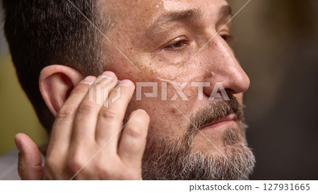 Close-up of mature man applying serum, moisturizer to cheek. Aging with care Close-up of mature man applying serum, moisturizer to cheek. Aging with care 127931665