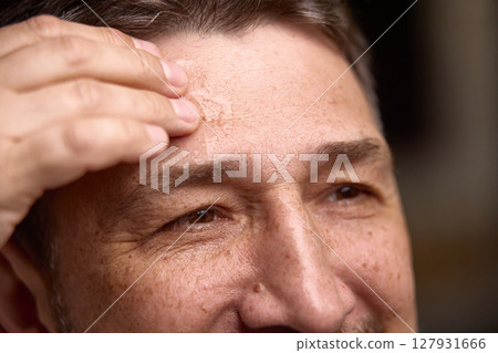 Beauty and aging. Mature man applying skincare product to forehead, close-up shot Beauty and aging. Mature man applying skincare product to forehead, close-up shot 127931666